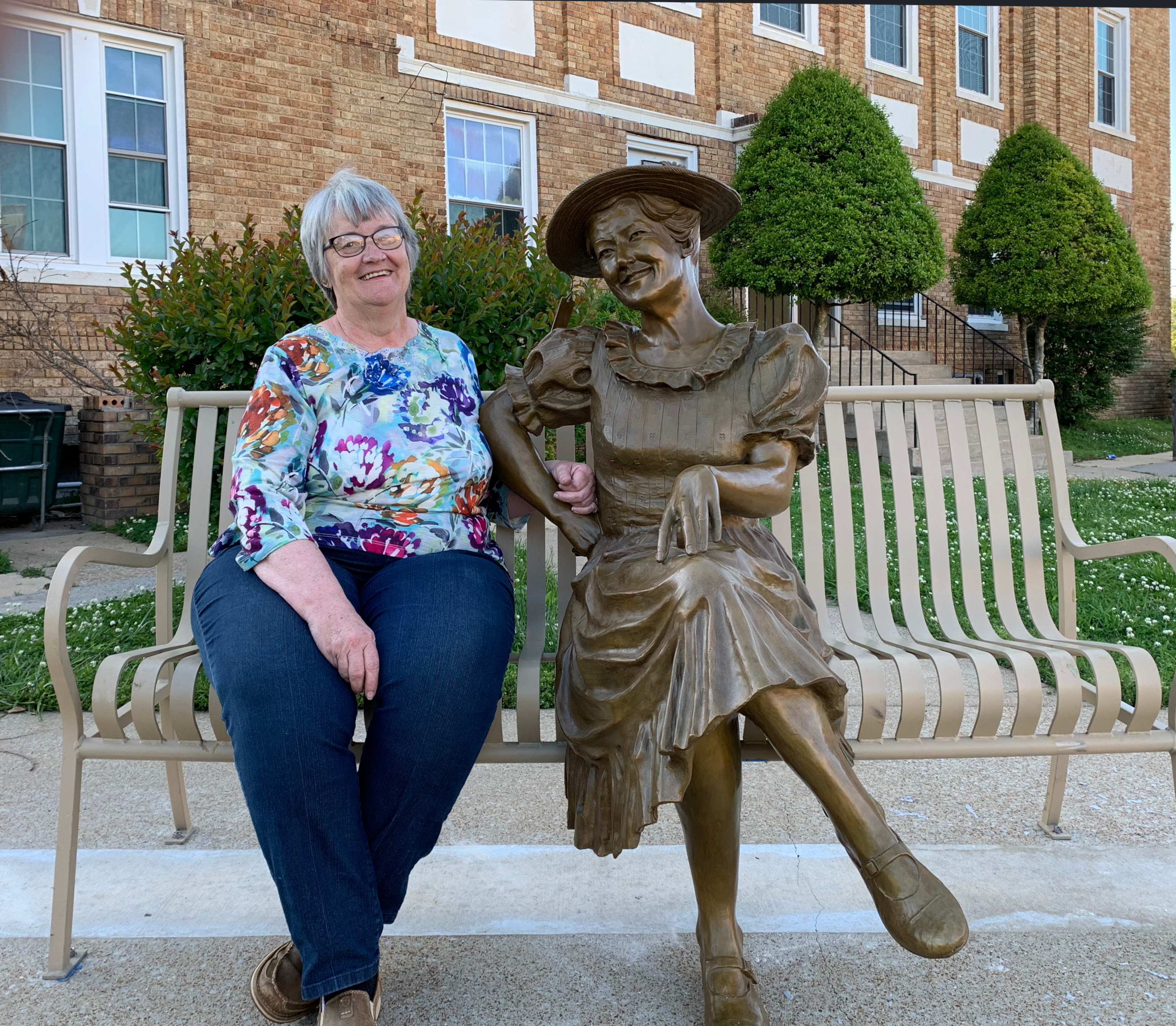 Mary Beth Pruett sitting with the Minnie Pearl Statue on the Courthouse lawn in Centerville